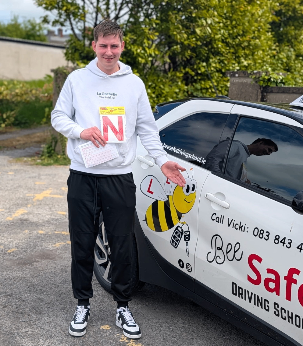 Bee Safe Driving School student standing beside the tuition car holding novice plates after passing